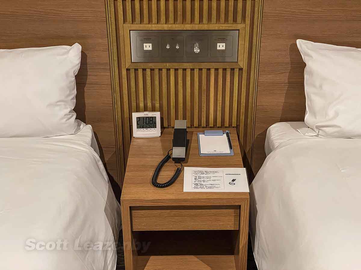 Tobu Hotel Narita bedside table with alarm clock, electrical outlets, and phone