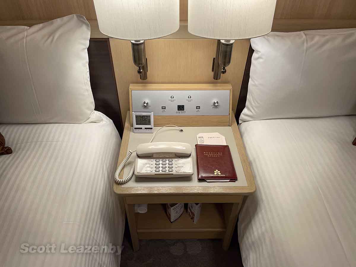 Nikko Hotel NRT bedside table with phone, alarm clock, and lighting controls